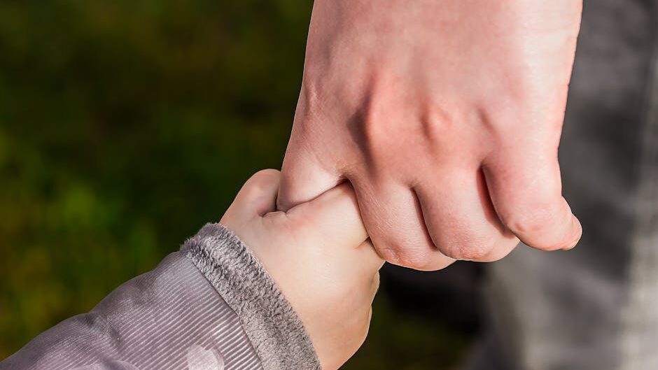 A close-up of a child and parent holding hands in a park, symbolizing love and trust.