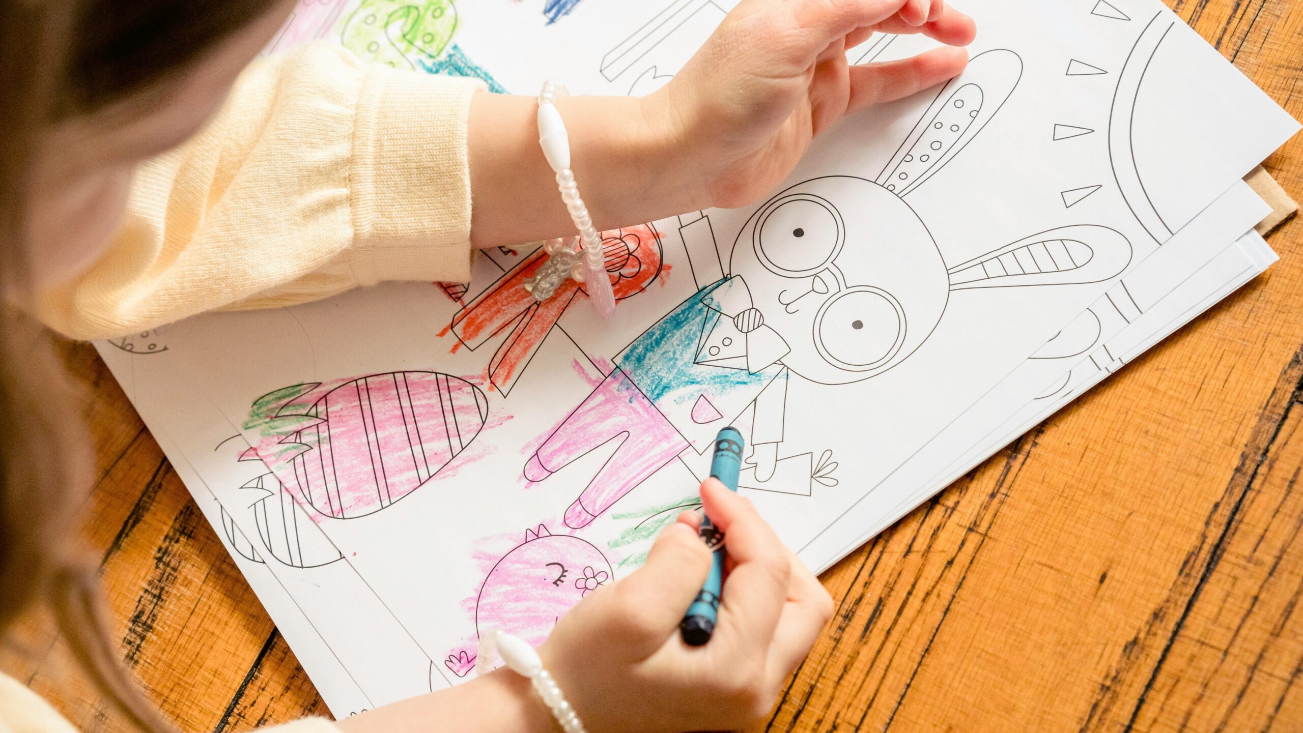 From above of crop unrecognizable girl in casual clothes drawing in coloring book in daylight